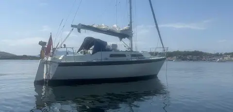 Westerly Merlin 28: afloat at anchor on calm water with blue sprayhood and boom cover
