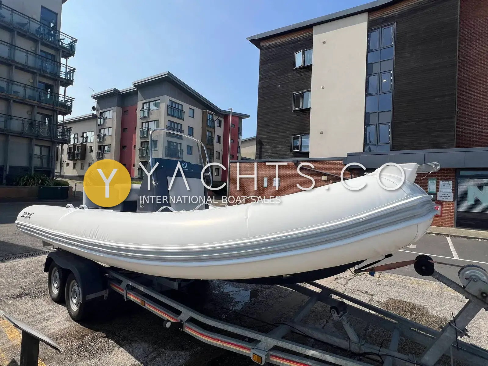 Zodiac Medline 580 Rib: grey-tubed RIB on a twin-axle trailer beside flats, seen from the bow quarter