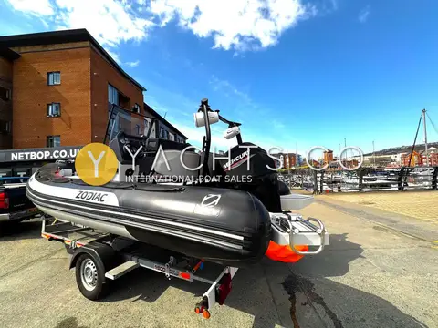 Zodiac Open 5.5 Rib: bow quarter view on the trailer by a marina, with covered outboard and swim platforms