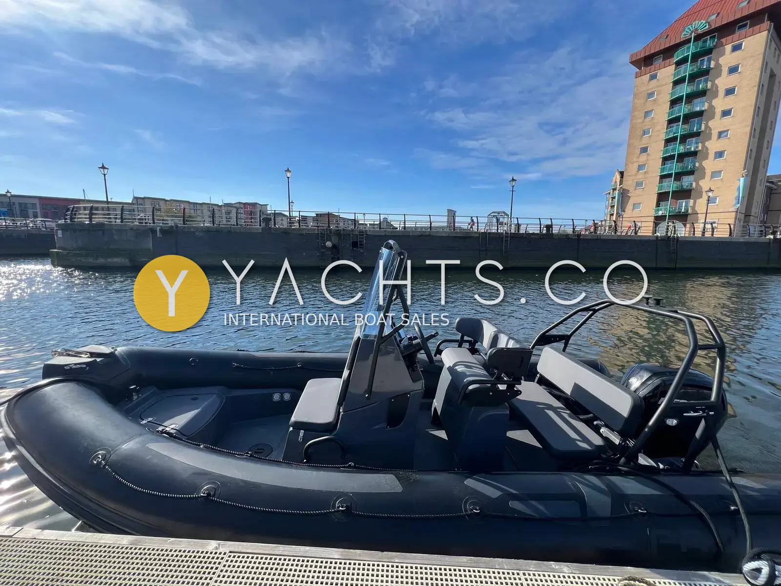 Zodiac Pro 5.5 Rib: dark grey RIB afloat in a marina beside a tall apartment block, console and roll bar visible
